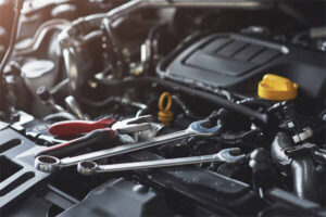 Close-up of a car engine surrounded by wrenches and tools, highlighting mechanical components and repair equipment.